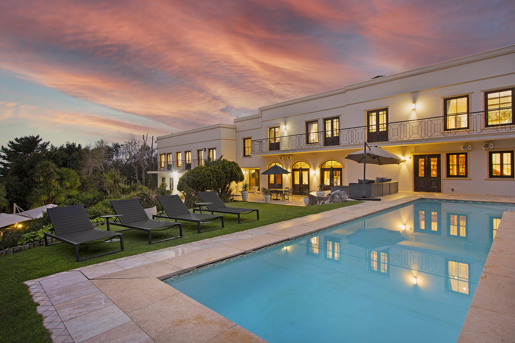 Lyonesse House illuminated at dusk beside its swimming pool